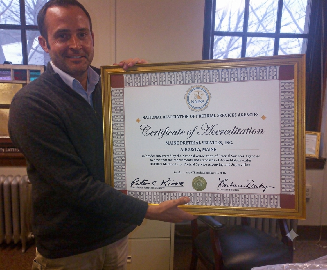 A man in a grey sweater holds a framed National Association of Pretrial Services Agencies (NAPSA) Certificate of Accreditation awarded to Maine Pretrial Services, Inc.